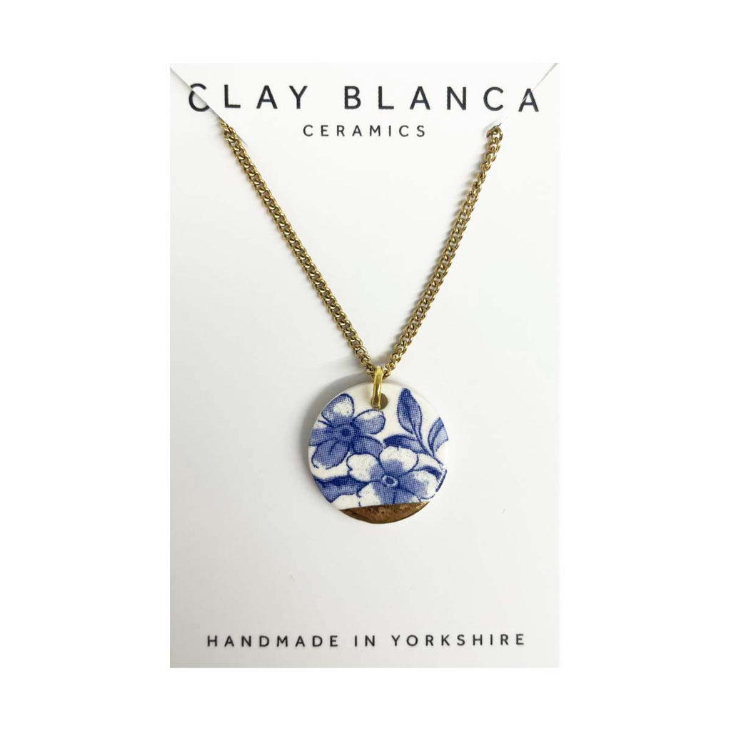 Blue floral porcelain necklace with round pendant and gold chain on a white background.