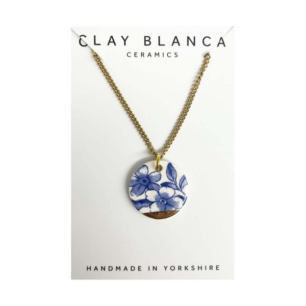 Blue floral porcelain necklace with round pendant and gold chain on a white background.