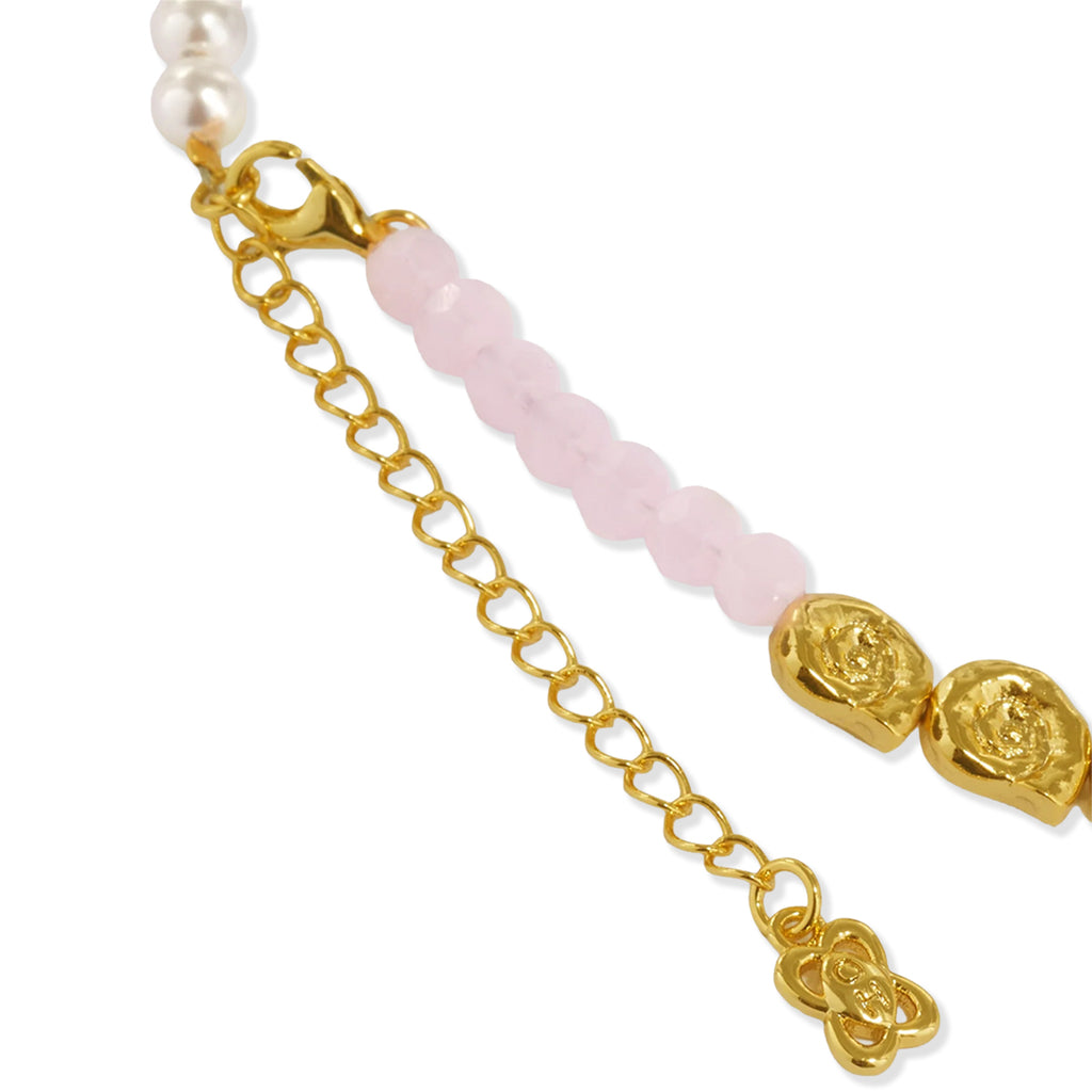 Close-up of a beaded bracelet with pale pink round beads, white pearl-like beads, gold-tone chain extender, and gold-tone decorative end pieces on a white background.