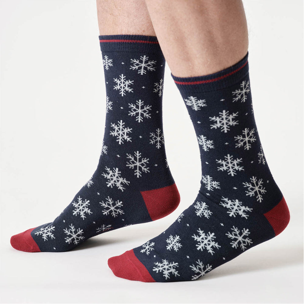 Navy socks with white snowflake patterns and red toes worn by a person on a light gray background