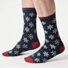 Navy socks with white snowflake patterns and red toes worn by a person on a light gray background