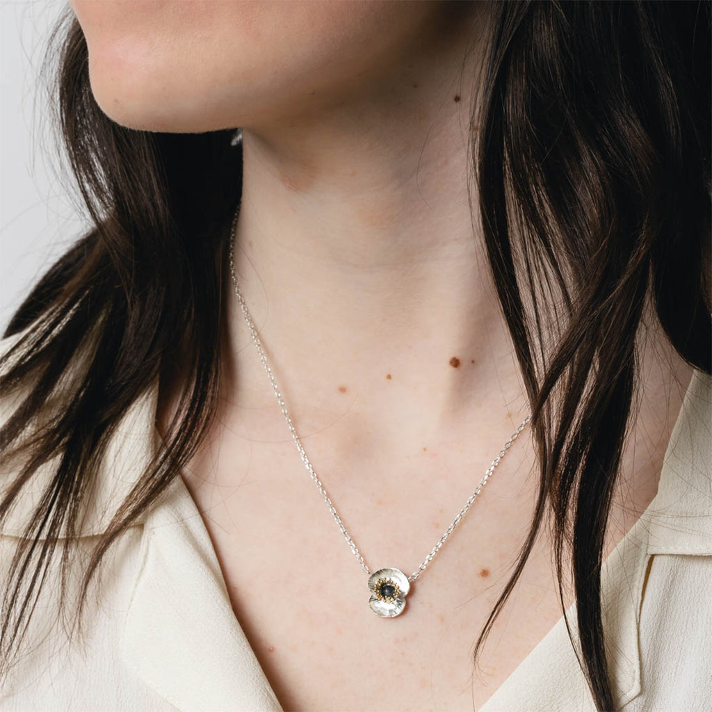 Close up of silver and gold poppy flower pendant necklace on model's neck. 