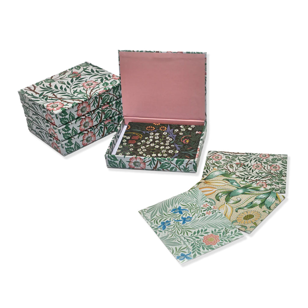 A notecard box set with a floral patterned exterior, shown closed in a stack and open to reveal a pink interior and a tray holding notecards of assorted Morris & Co wallpaper floral designs, against a white background.
