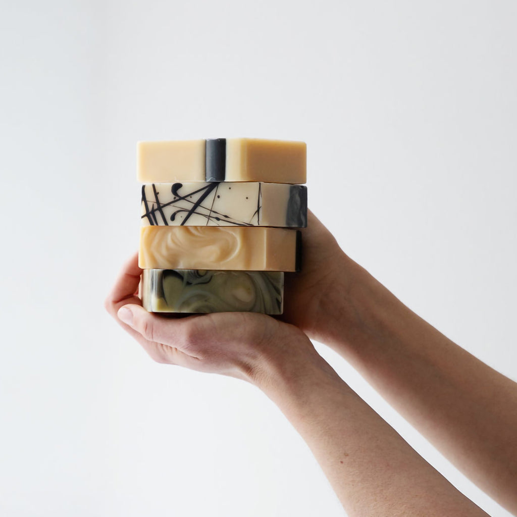 Hand holding a stack of marbled soap bars against a white background