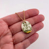 Gold chain necklace with a green and white pendant held in a hand against a white background