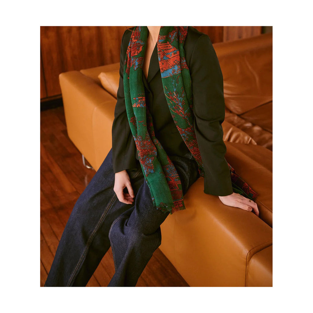Person wearing a green jacket and colourful green wool scarf sitting on a brown leather couch.