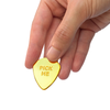 Hand holding a gold guitar pick with 'PICK ME' text against a white background