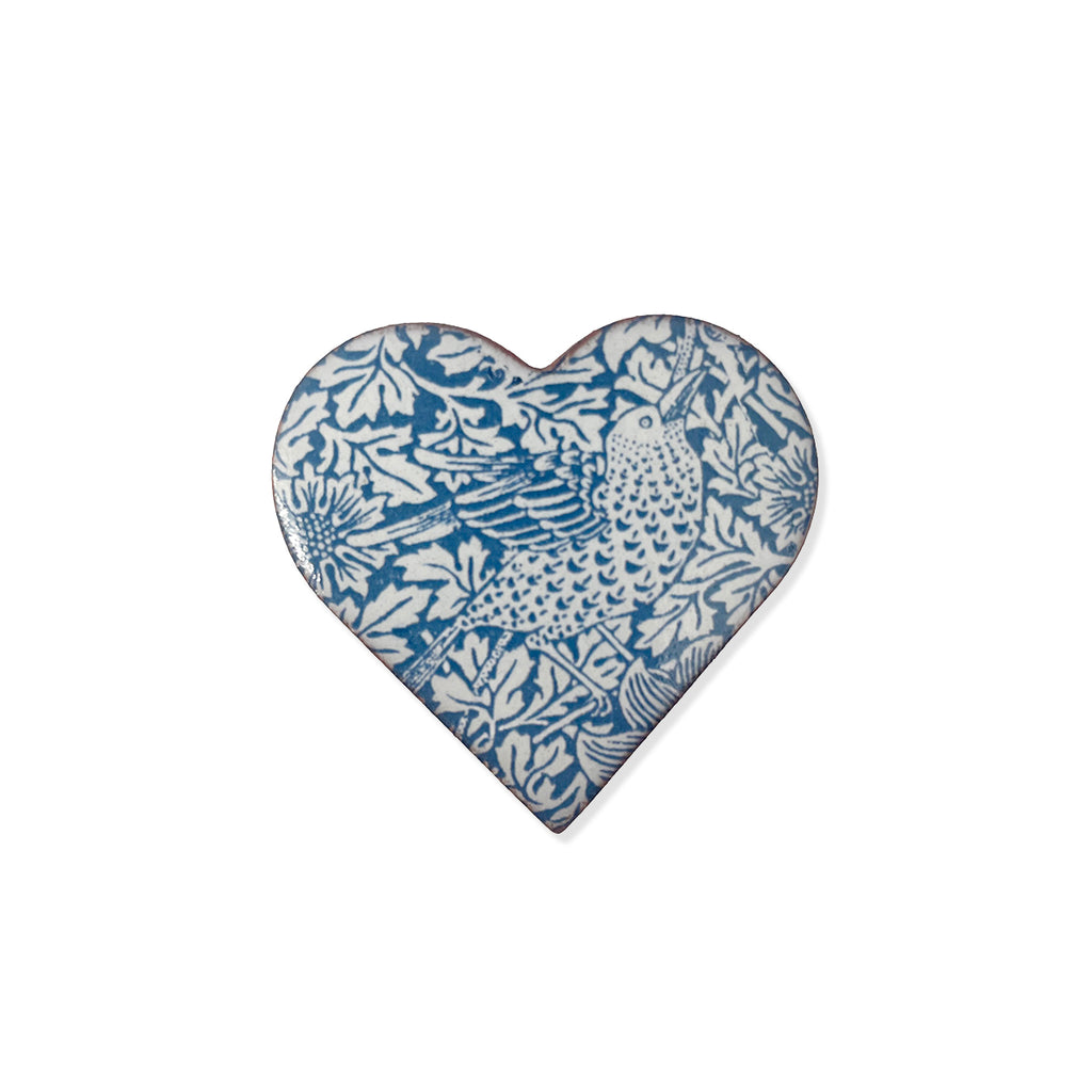 A heart-shaped ceramic pin brooch featuring a blue and white floral and bird pattern, shown against a plain white background.
