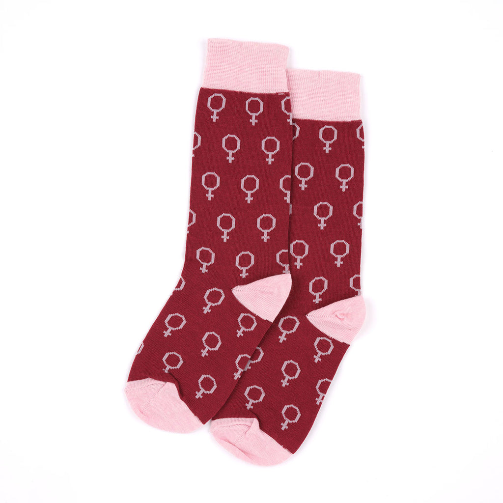 A pair of crew socks in burgundy with a repeating white female symbol pattern, featuring light pink heels, toes, and ribbed cuffs, displayed on a clean white background.