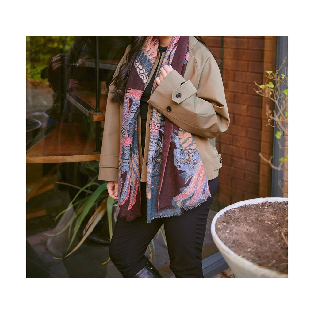 Person wearing the plum crane patterned wool scarf layered on top of a beige coat in an outdoor setting