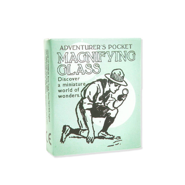 Green box with 'Adventurer's pocket magnifying glass / Discover a miniature world of wonders' text and boy scout kneeling on ground on a white background.