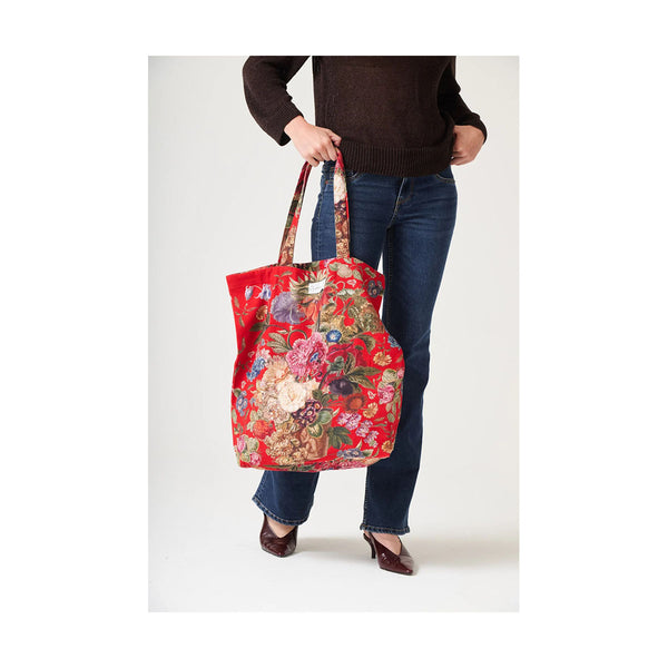 Person holding a red floral tote bag against a white background