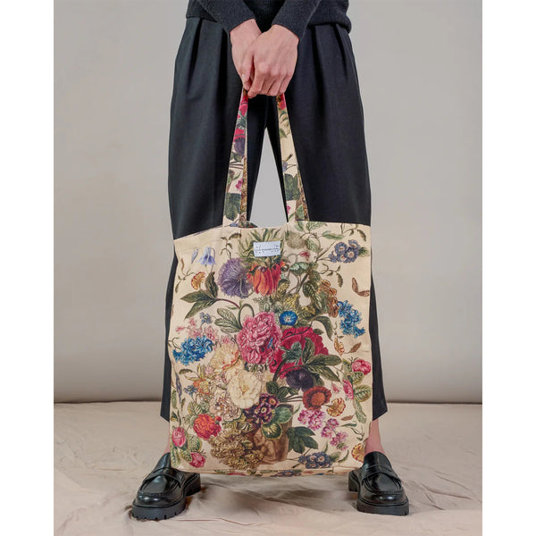 Person holding a floral tote bag against a neutral background