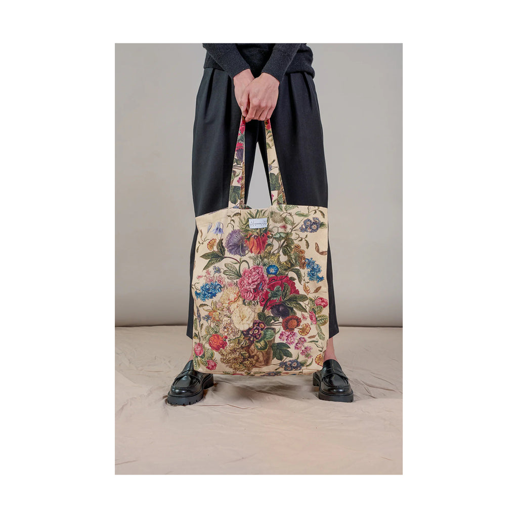 Person holding a floral tote bag against a neutral background