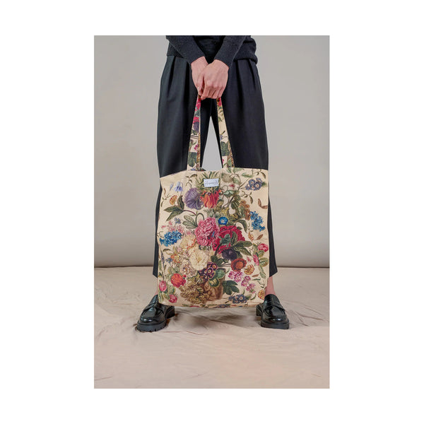 Person holding a floral tote bag against a neutral background