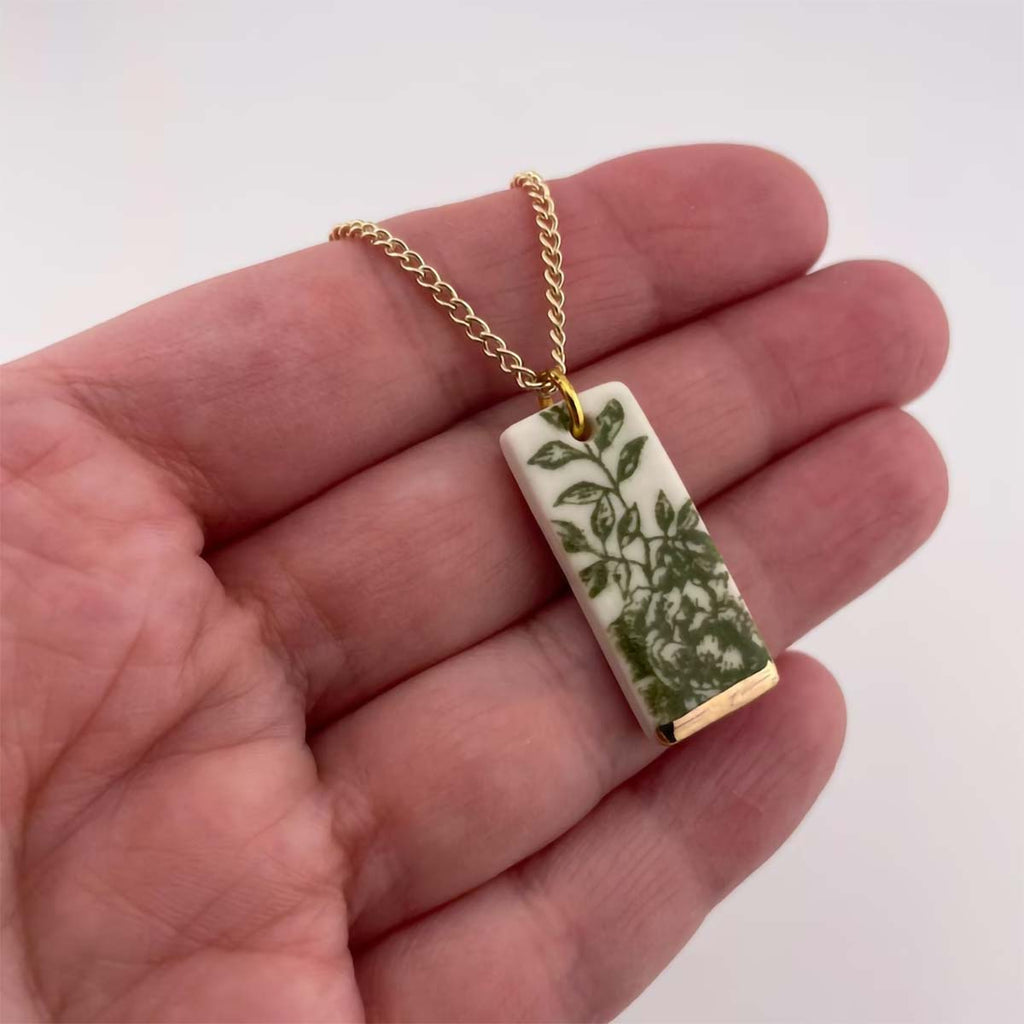 Close up of hand holding porcelain rectangle necklace pendant with green china pattern.