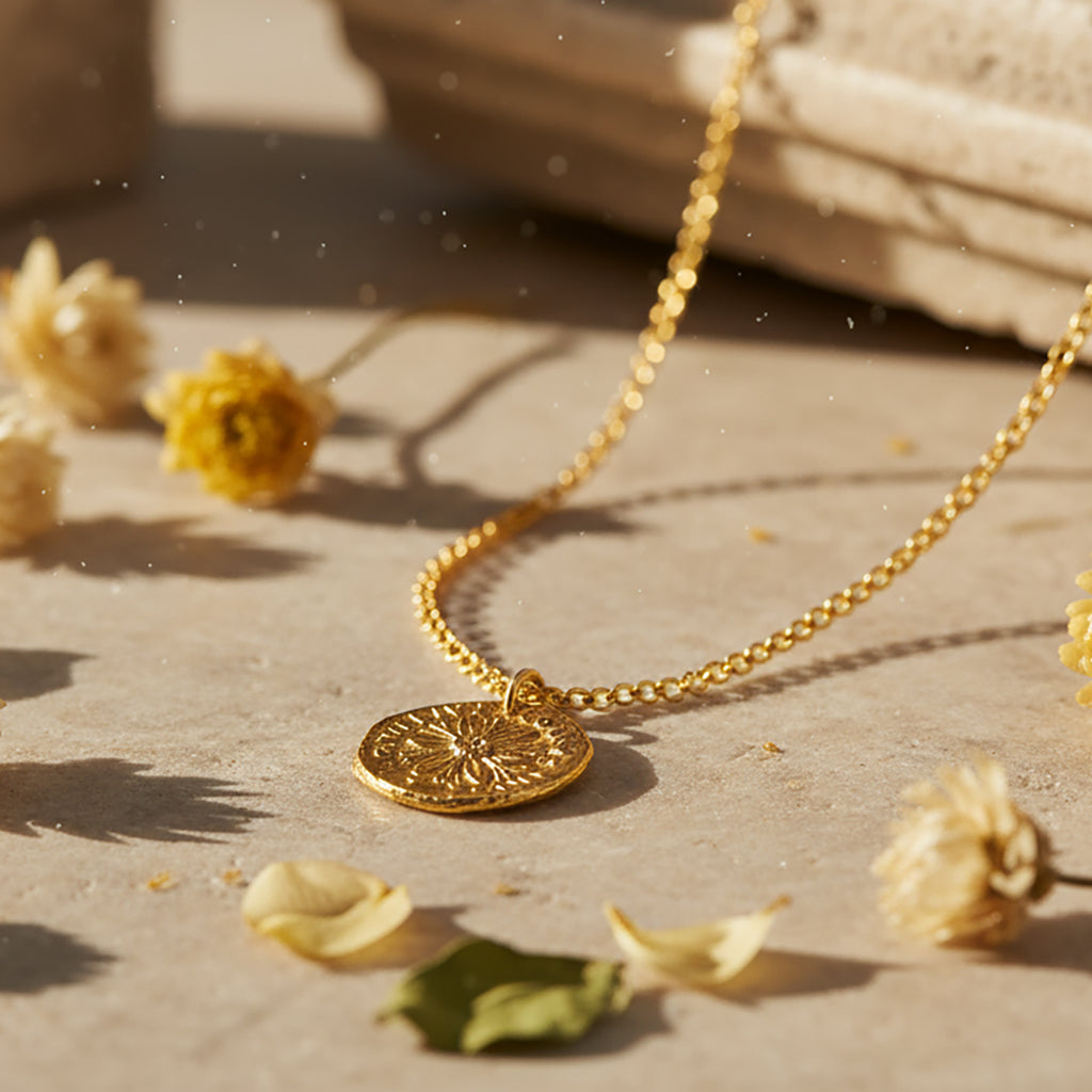 Gold necklace with a pendant on a surface with dried flowers