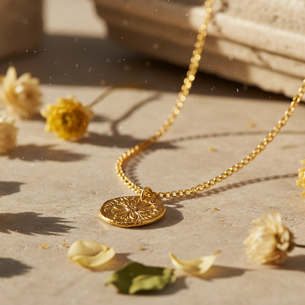 Gold necklace with a pendant on a surface with dried flowers