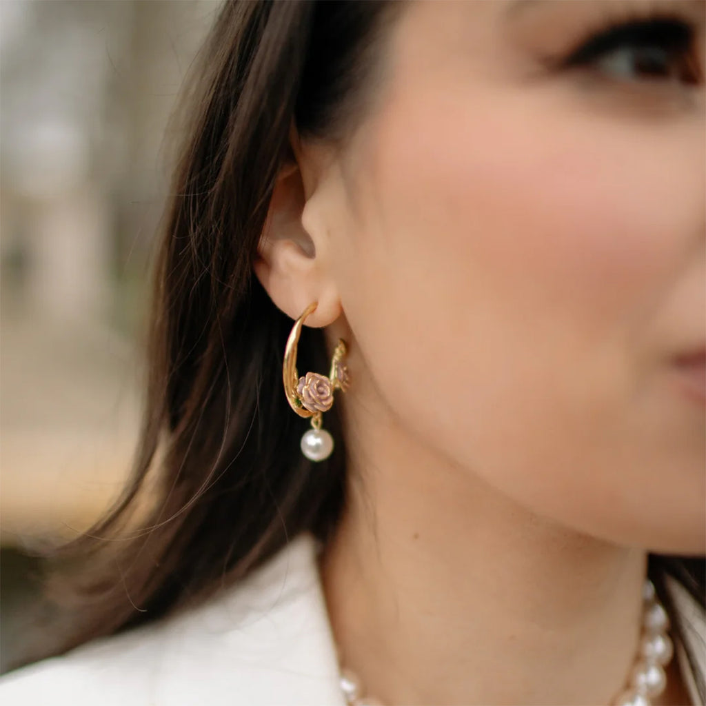 Close-up of a woman wearing gold hoop earrings with a pearl charm.