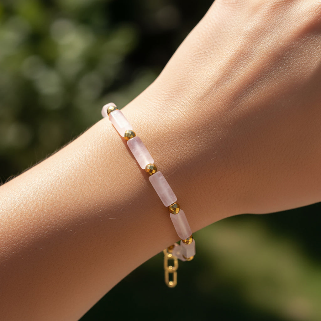 Close-up of a wrist wearing a pink beaded bracelet with gold accents against a blurred green background