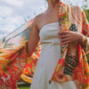 Model wearing orange floral fans patterned scarf over white dress 