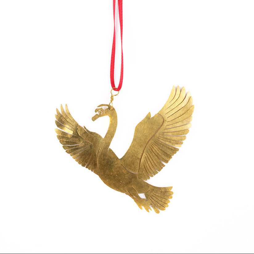 A gold-toned metal swan ornament with wings spread, hanging from a bright red ribbon on a plain white background.