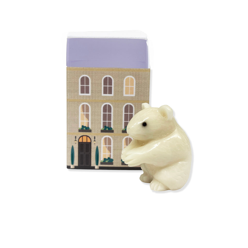 White carved miniature figurine of a mouse in front of matchbox with townhouse decoration on a white background.