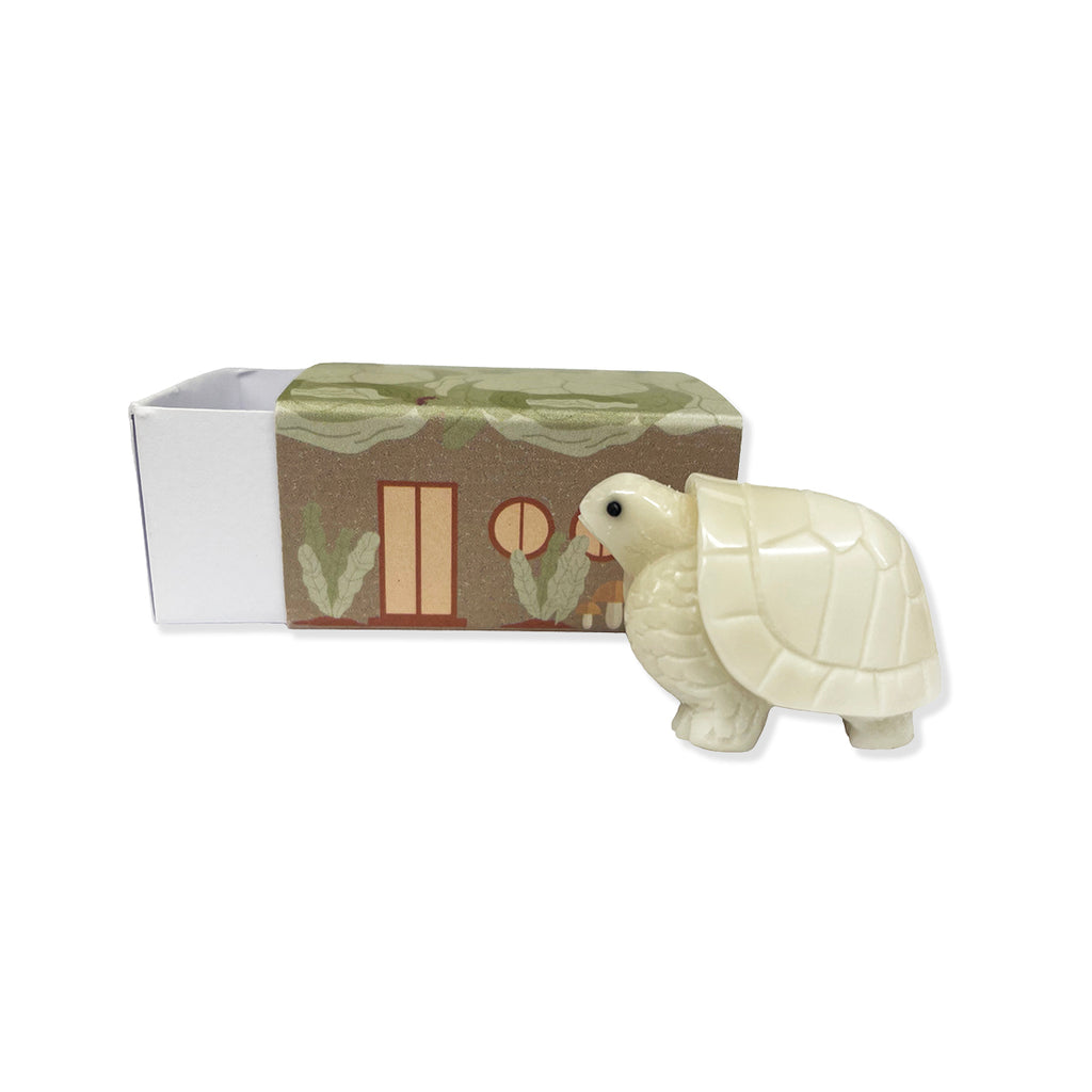 White tortoise figurine in front of a box with greenery design.