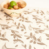 An off-white tablecloth with a repeating brown olive branch pattern, styled with a small bowl of walnuts and green apples in the upper left corner.