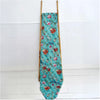 Floral-patterned teal cotton stitched throw blanket draped over wooden ladder against a white background