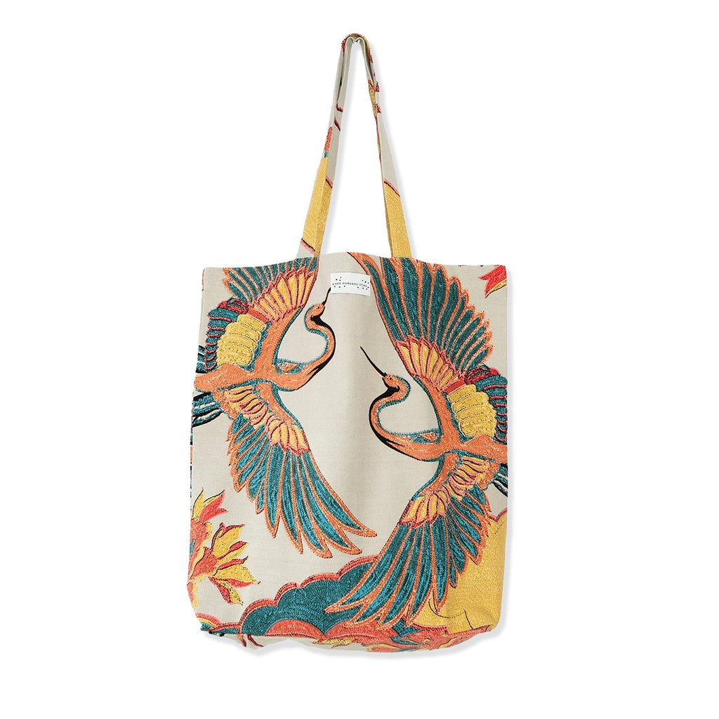 Canvas tote bag with stone cotton material and orange and red colourful crane bird printed pattern on a white background.