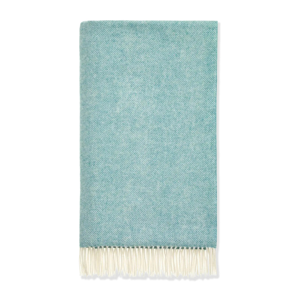 Wool throw in green/blue herringbone pattern with white tasselled edges on a white background.