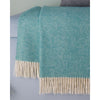 A teal and cream herringbone woven throw blanket with fringe, draped over a light blue sofa.