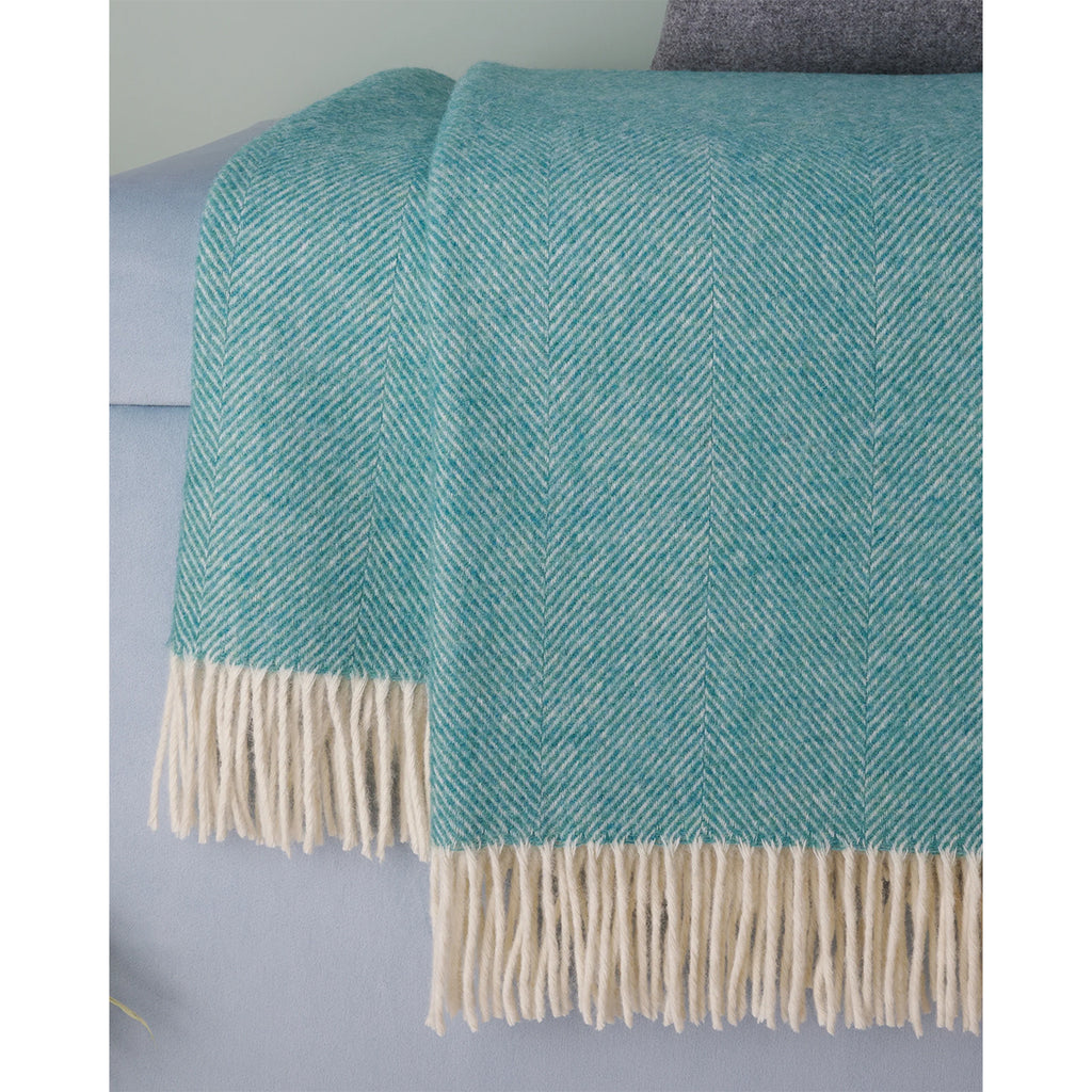 A teal and cream herringbone woven throw blanket with fringe, draped over a light blue sofa.