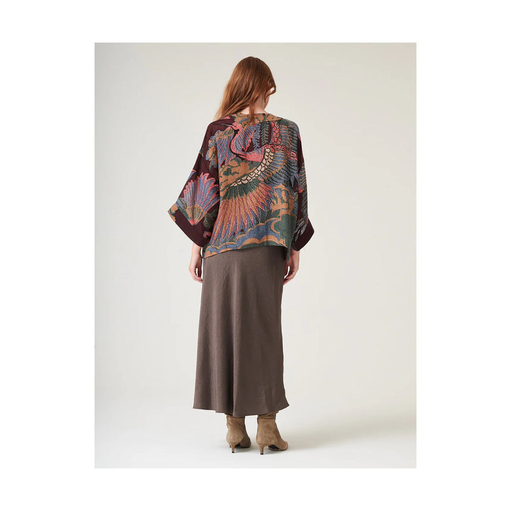 Woman wearing a patterned wool kimono and brown skirt with their back turned on a white background 