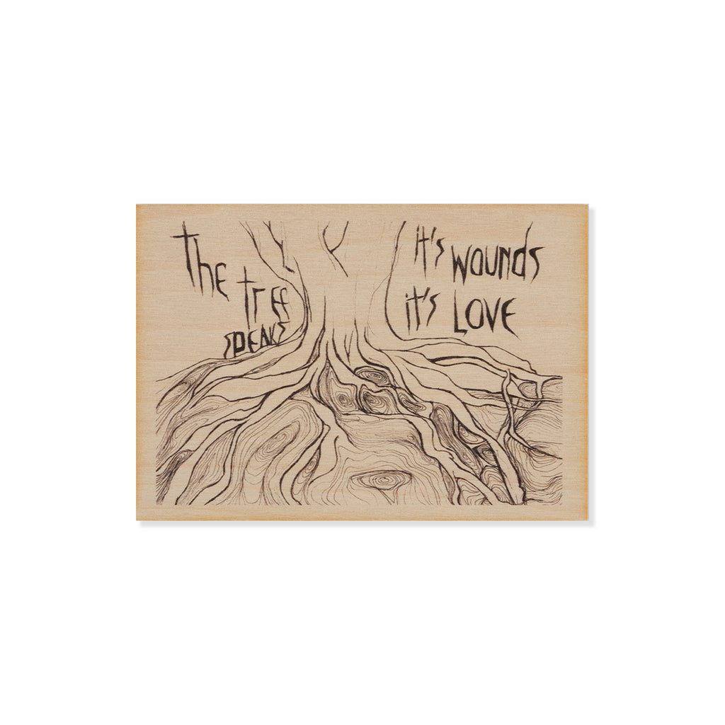 Wooden postcard with a tree design and text 'The Tree Speaks, Its Wounds, Its Love' on a white background