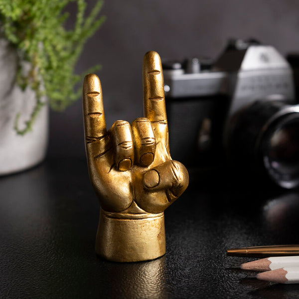 Bronze hand gesture sculpture on a dark surface with a blurred camera in the background