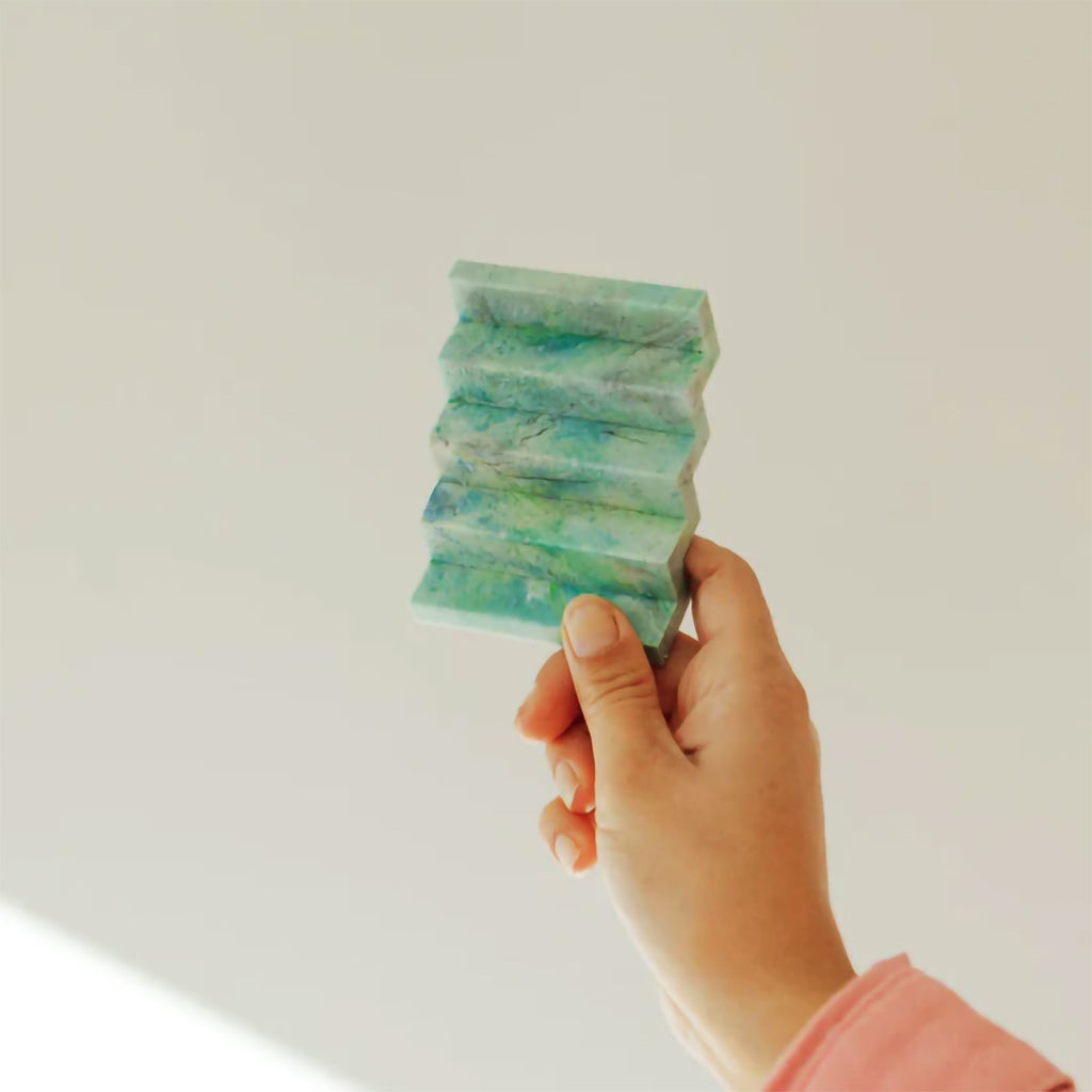 Hand holding green plastic recycled zig zag soap dish against a plain background